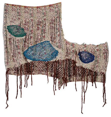Textile artwork featuring floral patterns and vibrant blue patches, with elongated fringe details cascading down the sides.