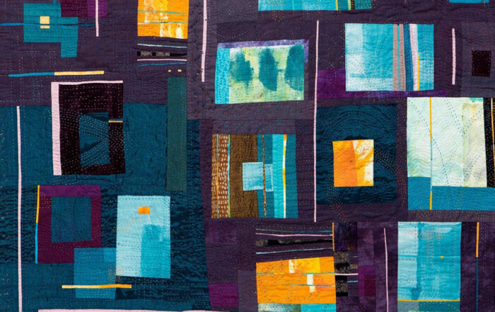 A vibrant quilt featuring a patchwork of teal, blue, and purple fabrics, with geometric shapes and textured stitching.