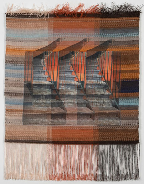 A textured woven tapestry featuring overlapping stair imagery in warm tones of orange, brown, and blue, with fringed edges.