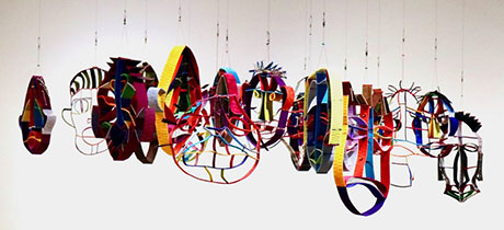 A colorful hanging sculpture featuring abstract masks in various shapes and patterns, creating a vibrant, artistic display. A colorful hanging sculpture featuring abstract masks in various shapes and patterns, creating a vibrant, artistic display.