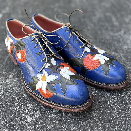 Vibrant blue leather shoes adorned with colorful floral and fruit designs, featuring intricate detailing and classic laces.