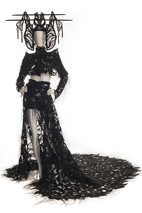 A dramatic black gown with intricate lace, featuring a high slit and majestic headpiece, displayed on a mannequin against a white background. A dramatic black gown with intricate lace, featuring a high slit and majestic headpiece, displayed on a mannequin against a white background.