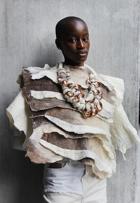 A model wears an artistic, layered felt top in shades of brown and cream, adorned with a bold, decorative necklace. A model wears an artistic, layered felt top in shades of brown and cream, adorned with a bold, decorative necklace.