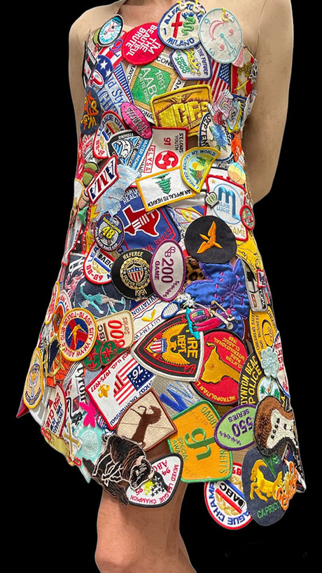 A colorful dress adorned with numerous vintage patches and badges, showcasing various symbols and logos against a black background. A colorful dress adorned with numerous vintage patches and badges, showcasing various symbols and logos against a black background.