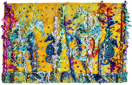 Colorful textile art featuring seahorses and vibrant patterns on a sunny yellow background, adorned with ribbons and beads.
