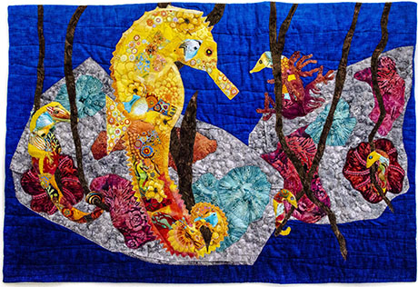 Colorful fabric art featuring vibrant seahorses and coral against a deep blue background, showcasing intricate patterns and textures.