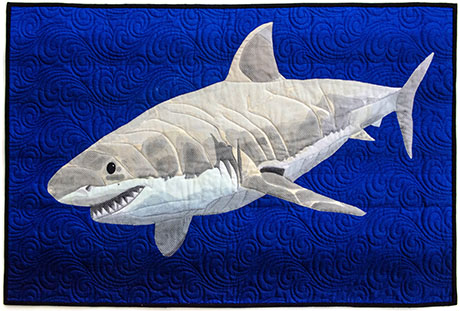 A quilted artwork of a great white shark swimming against a deep blue textured background.