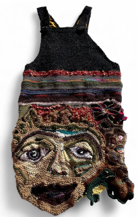 The Many Mother’s Maternity Dress has overalls on top, a crocheted striped bodice, and stretching skirt made of faces, creatures, and symbols of transformation.