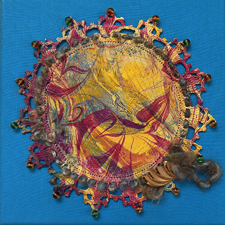Colorful textile art on blue background features a swirling yellow, red, and purple central pattern. Edged with pink lace and beads, evoking vibrancy.