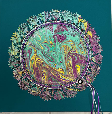 A vibrant circular artwork with swirling patterns in teal, purple, and yellow, bordered by intricate lace and beads on a deep teal background.