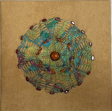 Colorful crocheted mandala with a central orange bead and brown accents on a textured beige background, conveying warmth and intricacy.