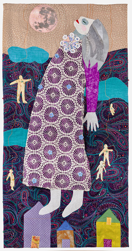 Fabric artwork depicting a large, abstract woman in a patterned purple dress, gazing upward. Surrounded by small figures, houses, and a full moon, it conveys a whimsical, dreamlike tone.