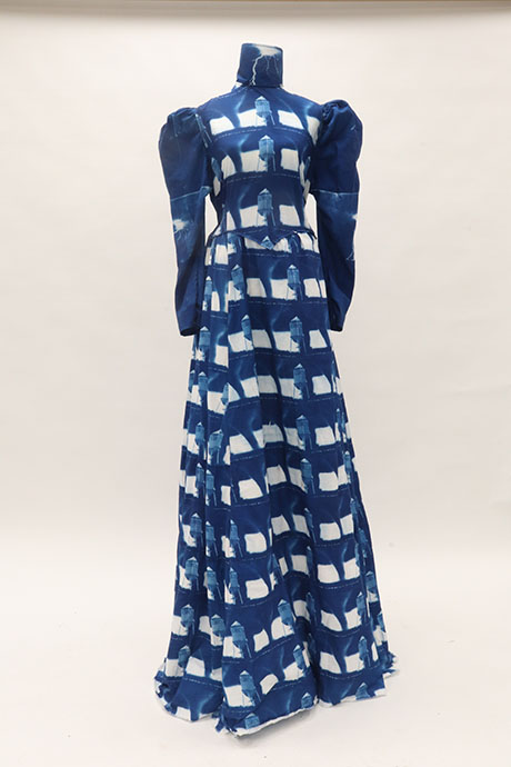 Blue and white long dress with high collar and puffed sleeves, featuring a bold pattern of watertowers and squares, displayed against a plain background.