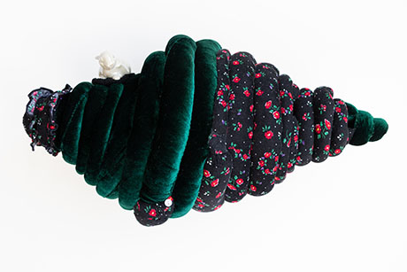 A plush, conical sculpture with green velvet and floral patterns resembles a soft Christmas tree. A small white bear sits atop, adding whimsy.