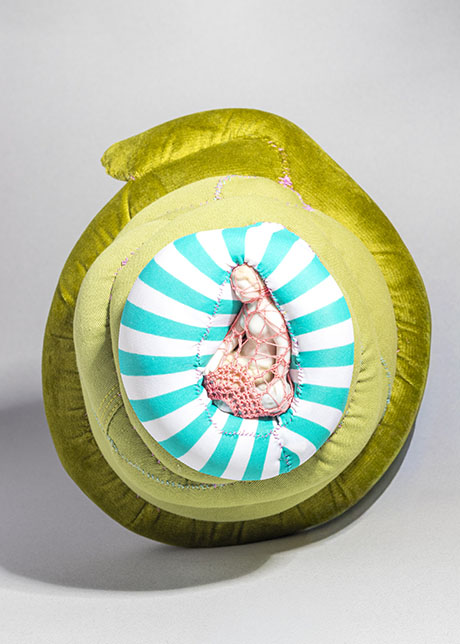 A whimsical, abstract sculpture featuring a green, spiral-shaped outer layer, with an inner section of teal and white stripes, and textured pink elements.