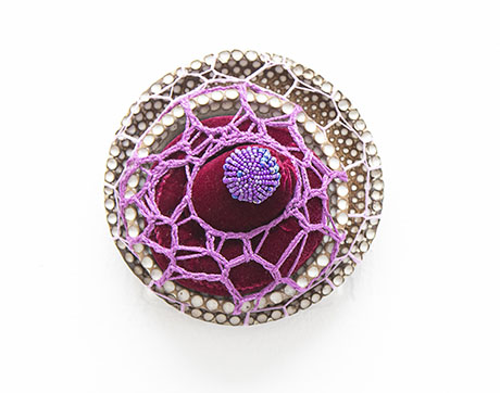 A handcrafted art piece featuring a circular design with a maroon center, decorated with a purple net pattern and surrounded by a beaded border.