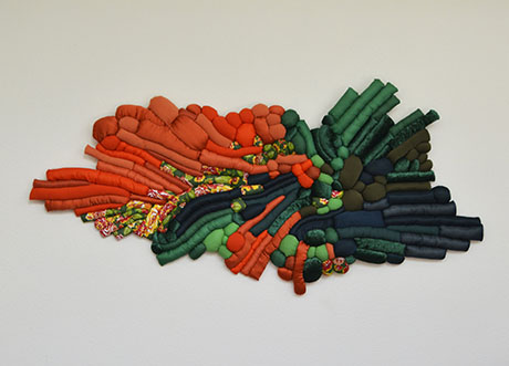 Abstract textile art featuring a mix of organic shapes and colors. Predominantly orange, green, and dark blue elements create a textured, flowing design.