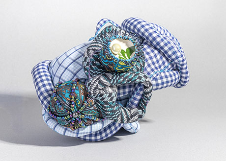 A colorful, abstract textile sculpture featuring blue checkered fabric intertwined with patterned, beaded elements, conveying a feeling of intricate creativity.