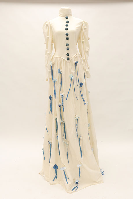 Elegant white gown with long sleeves, featuring blue buttons down the front. Blue and white flower details cascade down the skirt, adding a delicate touch.