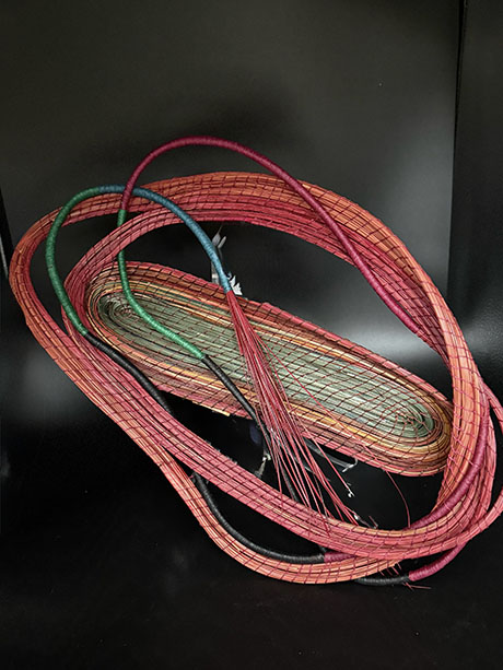 Coiled colorful cables with woven textures in hues of red, orange, green, and blue lie in a loosely piled arrangement against a black background.