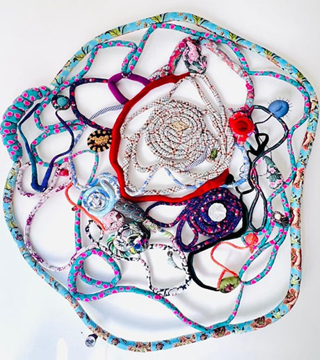 A colorful, tangled web of various patterned ropes and strings on a white background, forming an intricate, abstract star-like design.