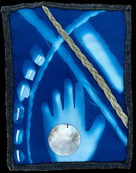A blue textile art piece features a hand silhouette, thin light streaks, braided fibers, and a round shell. The composition evokes a sense of mysticism.