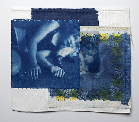 Fabric collage with two cyanotype images, one of a person resting, overlayed on textured cloth. Edges have floral patterns in yellow and green.