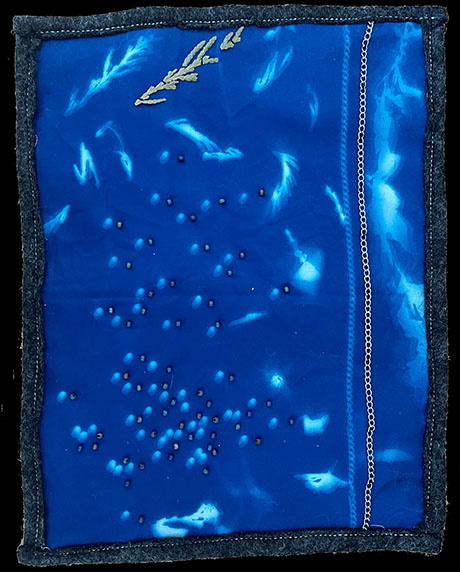 Blue textile art piece, featuring abstract white leaf patterns, scattered small beads, and a vertical silver chain on the right. Artistic and tranquil.