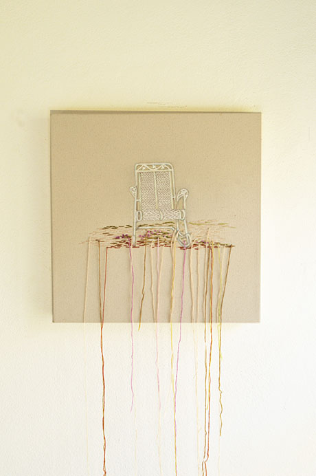 Embroidery art by Nereida Dusten of a chair on fabric canvas with colorful threads hanging down against a plain wall background. Embroidery art by Nereida Dusten of a chair on fabric canvas with colorful threads hanging down against a plain wall background.