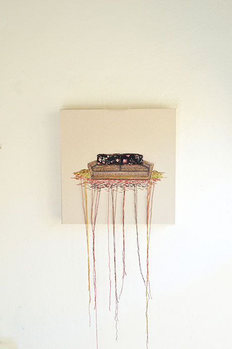 Embroidered artwork of a sofa with floral cushions, with colorful threads hanging down on a plain white wall. Embroidered artwork of a sofa with floral cushions, with colorful threads hanging down on a plain white wall.