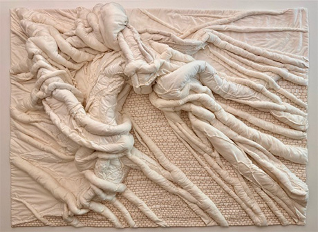 Abstract textile art piece with intertwined, tubular, padded fabric shapes in cream tones on a textured beige fabric background. Abstract textile art piece with intertwined, tubular, padded fabric shapes in cream tones on a textured beige fabric background.